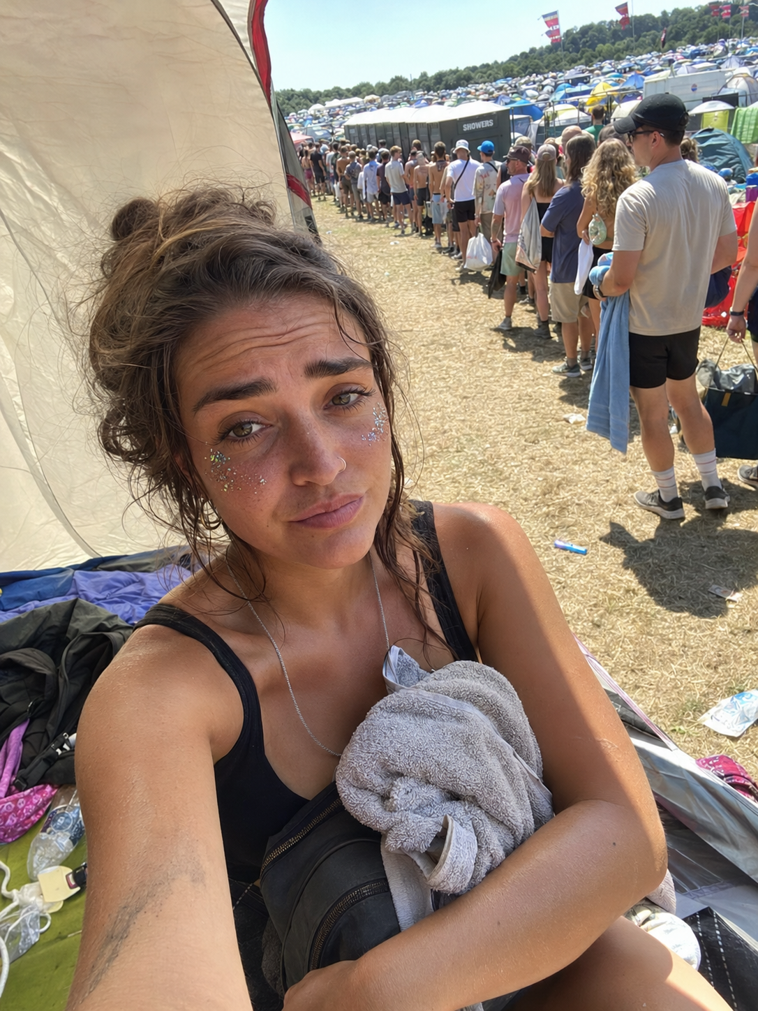 Festival-goer at her tent with the shower queue in the background